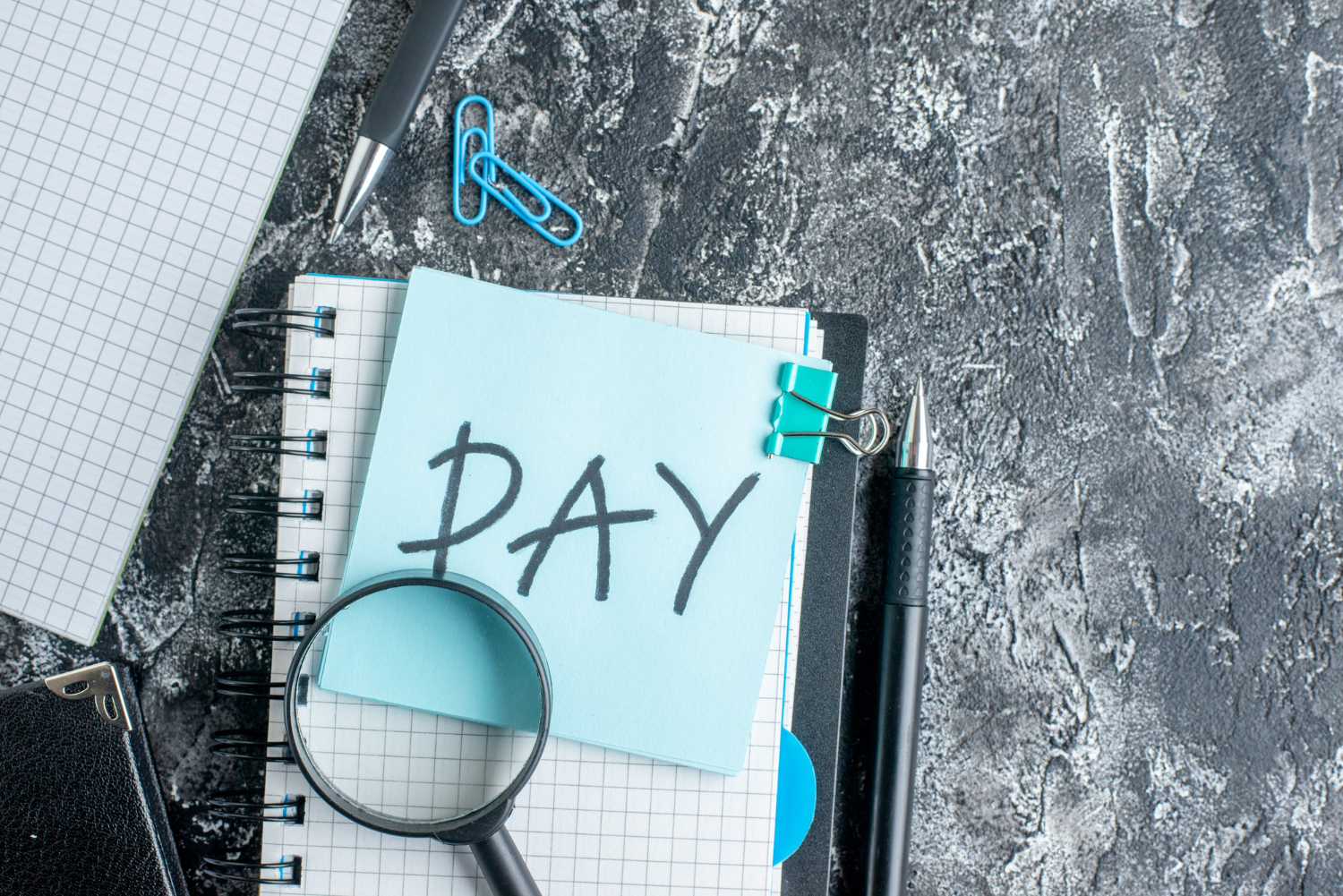 Payroll note with pens, notebooks, and a magnifying glass